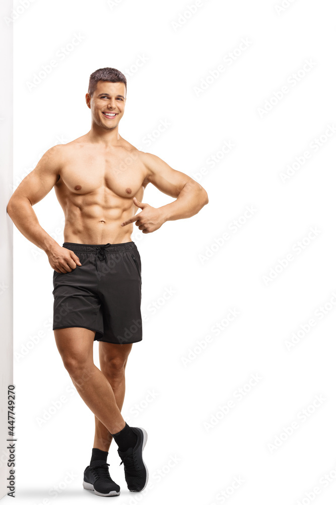 Full length portrait of a smiling shirtless man wearing shorts and pointing at his abs Full length portrait of a smiling shirtless man wearing shorts and pointing at his abs