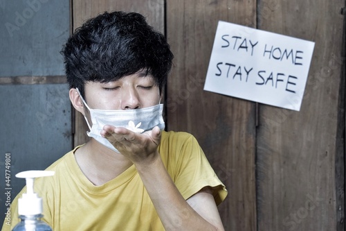 Southeast Asian, Chinese and Myanmar young man with cold flu gets loss of smell called anosmia. He wears surgical mask and smells scent of jasmine flower. photo