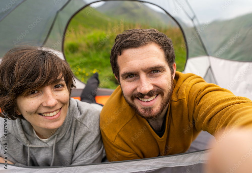 Happy couple inside a tent taking a selfie and enjoying a romantic vacation camping in Scotland