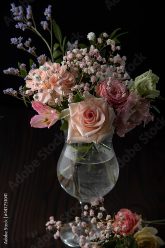 Flowers in a vase on a dark wooden background. A glass of water. Roses. Interior decor. Pastel colors.