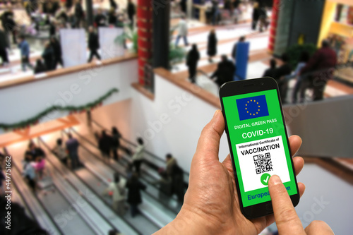 A man in a shopping mall holds a smartphone with the European Union digital green pass for Covid-19 in his hand. Safety concept for Coronavirus and the Green pass