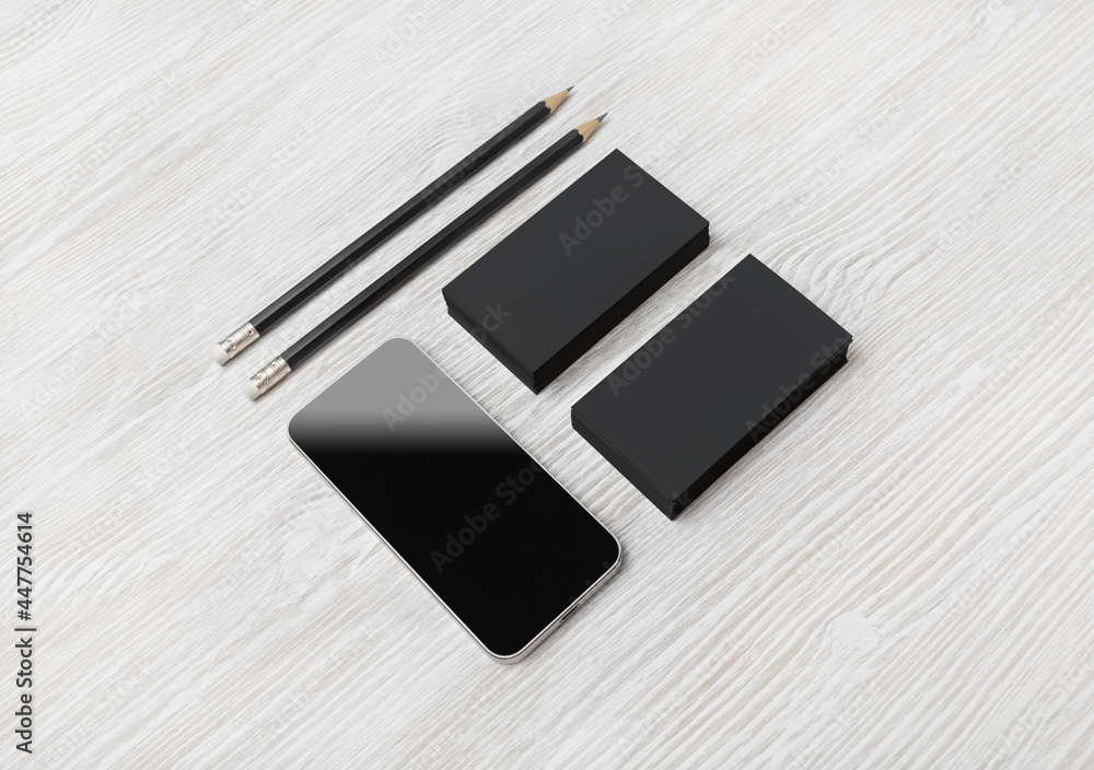 Smartphone, blank black business cards and pencils on light wooden background. Blank branding mockup.