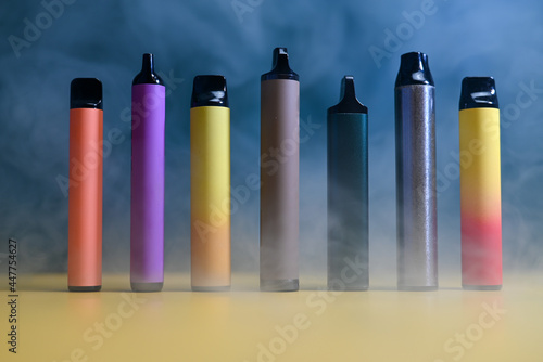 multicolored vape electronic cigarettes on dark green background in smoke