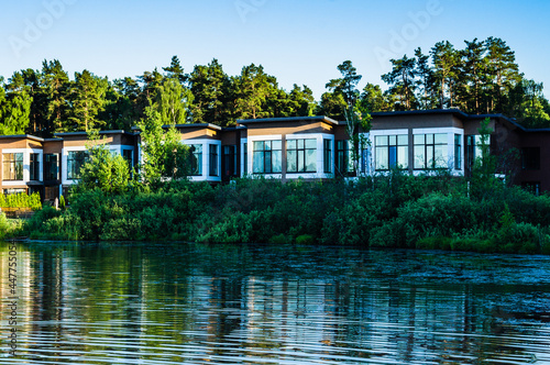 Contemporary houses next to lake and trees. Typical facade of a modern town suburban house near the pond © Konstantin