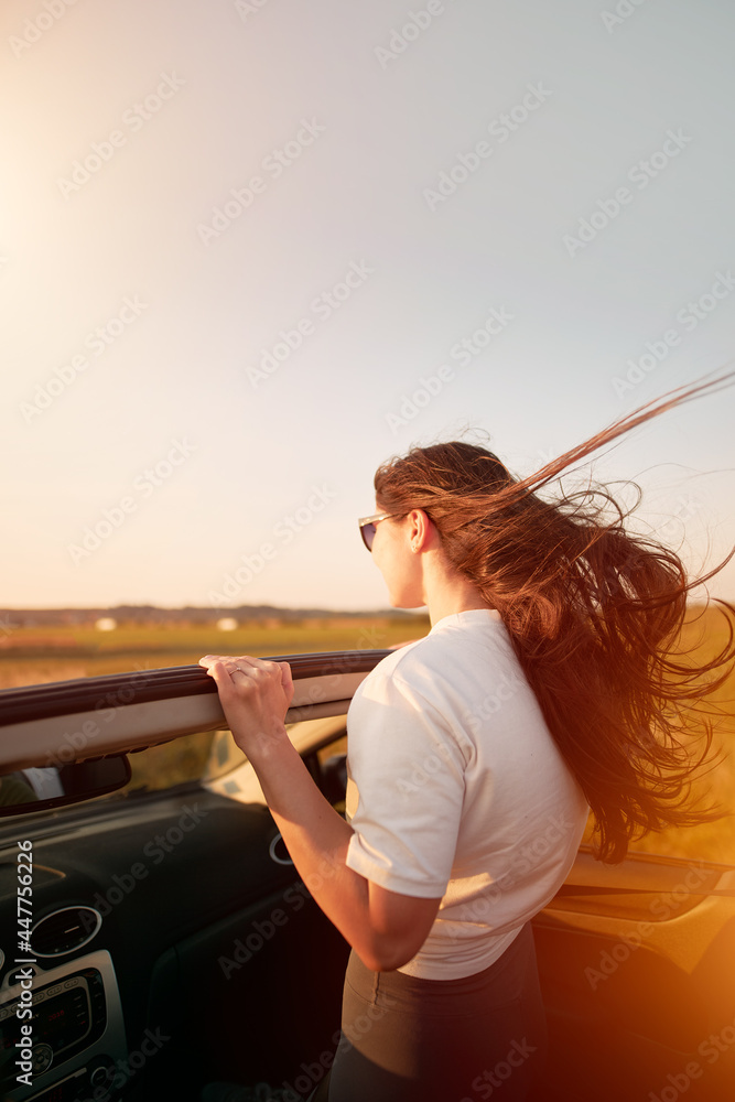 Attractive smiling woman wearing sunglasses in a convertible car. Concept of summertime journey and adventures by cabriolet car. Attractive smiling woman wearing sunglasses in a convertible car. Concept of summertime journey and adventures by cabriolet car.