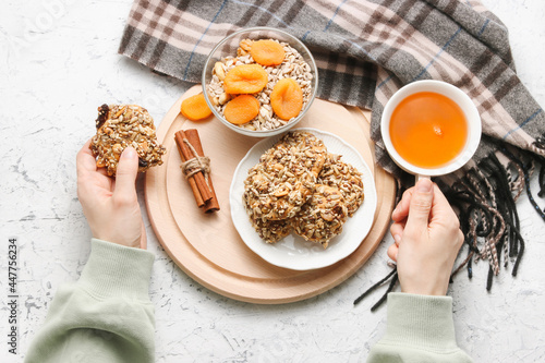 woman hands hold healthy cookie and cup of tea, homemade cookies made from dried fruits, sesame, sunflowers seeds, flaxseed and nuts, decorated with autumn scarf top view