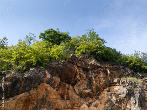 Yellow rock cliff with vegetation on top against blue sky