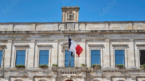 Фотография An old building facade of the city hall ( Mairie) in Gravelines, France stating in French  liberty, equality, fraternity , which is the national motto of France, with a French flag