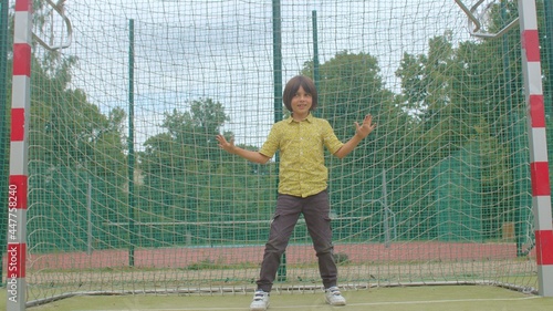 A teenager with long hair stands at the football goal. Prepares for a blow, makes body movements. He spread his arms.