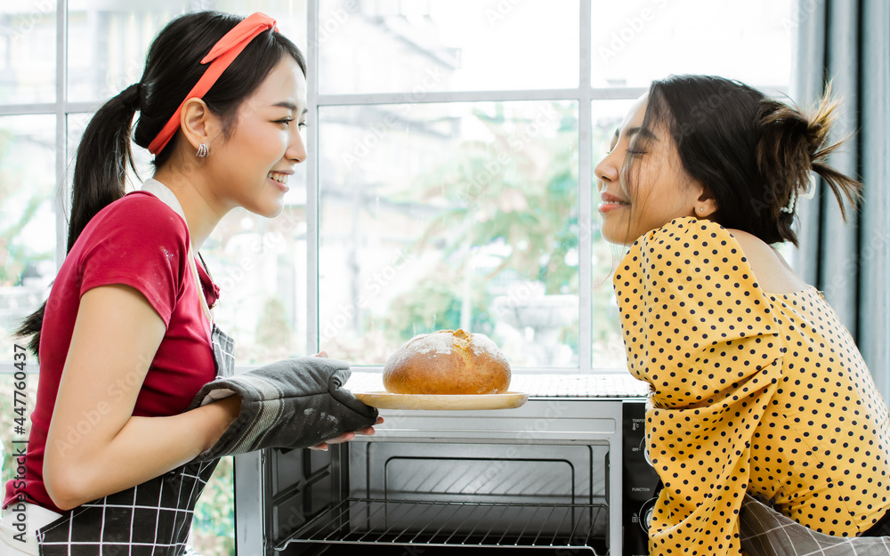 Φωτογραφία Two Asian beautiful adorable women or friends wearing aprons, smiling with happiness, cooking and serving baked bread in kitchen at cozy home as hobby on weekend