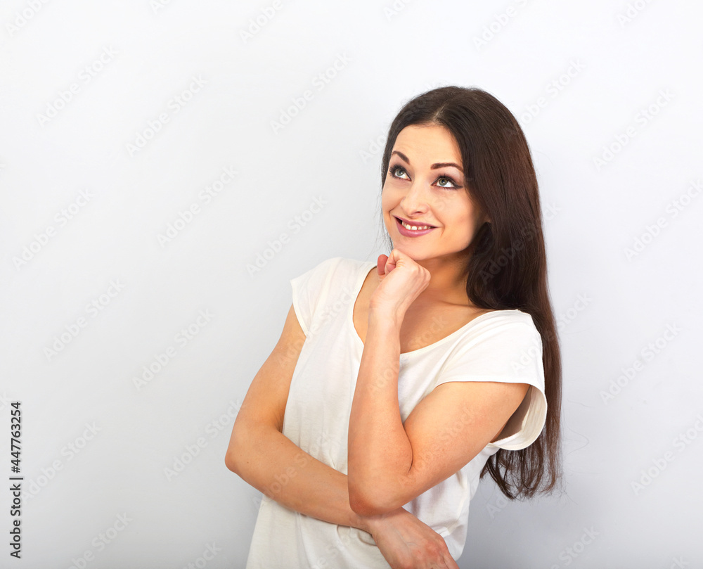 Beautiful young casual cute smiling woman on blue background looking up and thinking. Closeup portrait Beautiful young casual cute smiling woman on blue background looking up and thinking. Closeup portrait