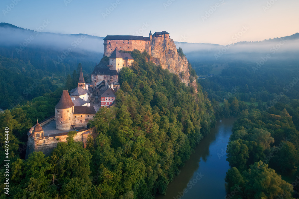  Aerial view of Orava Castle  situated on a high rock above Orava river, illuminated by rising sun, surrounded by deep forest and foggy mountains. Castles of Slovakia.
