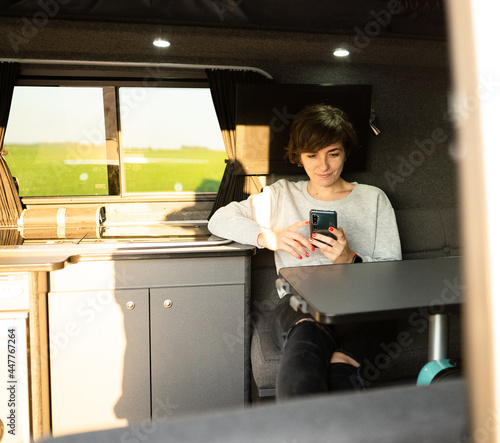 Photo of an attractive young female using her phone while sitting in a sofa inside of a campervan