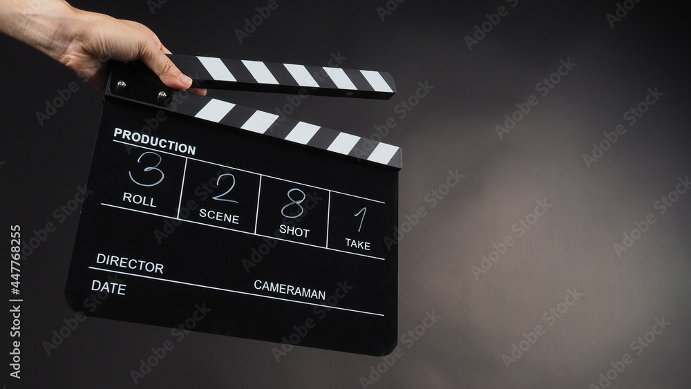 A hand is holding black clapper board or movie slate use in video production, movie, film, cinema industry on black background. It has written in number.