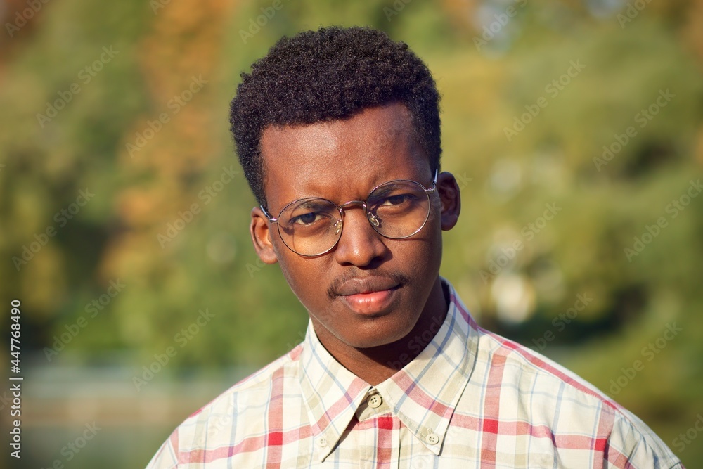 Close up portrait of unhappy serious angry disappointed annoyed dissatisfied black guy, young handsome African Afro American ethnic man in shirt and glasses looking at camera outdoors in autumn park Close up portrait of unhappy serious angry disappointed annoyed dissatisfied black guy, young handsome African Afro American ethnic man in shirt and glasses looking at camera outdoors in autumn park