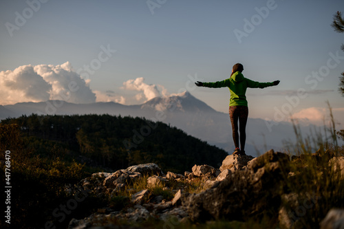 great rear view of woman with outstretched arms to sides against beautiful mountain landscape