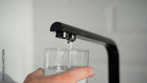 Close-up frame of drinking water being filled into a glass from the tap in the kitchen. Man's hands. Water flow into a transparent clean glass 