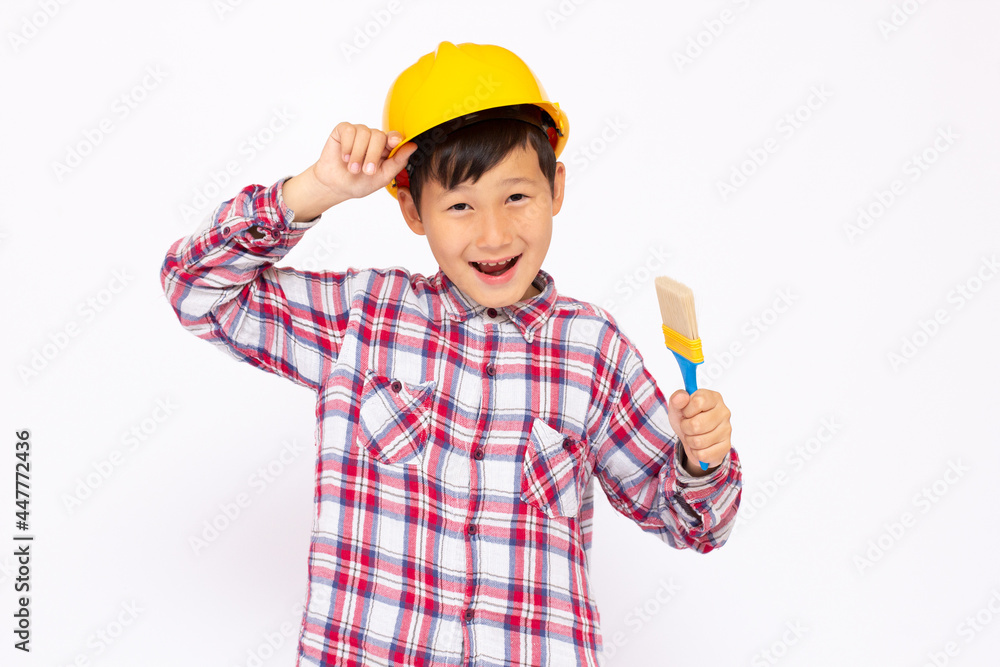 Little kid as a construction worker wearing yellow helmet with a paintbrush in his hand..White background studio picture. Little kid as a construction worker wearing yellow helmet with a paintbrush in his hand..White background studio picture.