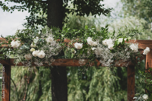 Wedding arch on boho style with white flowers in park.