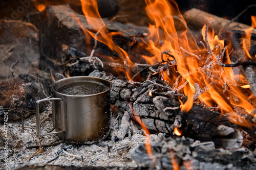 close-up of a steel camping mug with water by the fire flame