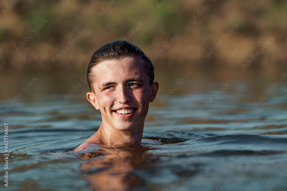 Fototapeta premium smiling young attractive man swims in a river or lake, enjoys and refreshes himself from swimming. The freshness wild nature. Relaxation and active summer vacation. Swimming skills. Dive into water