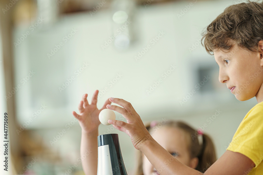 Curious boy and girl conducting a physical experiment called floating ball with a hairdryer and a plastic pink ball at home in the kitchen. Children are happy and laughing and jumping merrily Curious boy and girl conducting a physical experiment called floating ball with a hairdryer and a plastic pink ball at home in the kitchen. Children are happy and laughing and jumping merrily
