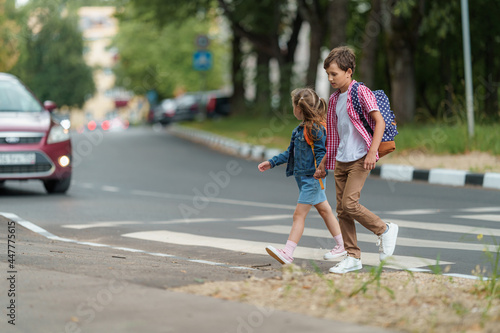 girl and boy with backpacks carefully cross road on pedestrian crossing on their way to school. Traffic rules. Walking path along zebra in city. concept of pedestrians crossing pedestrian crossing.