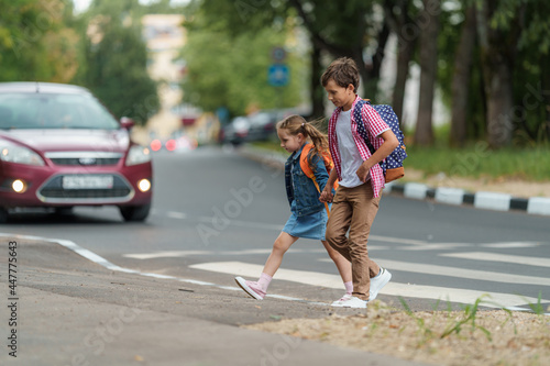 Fotografiet girl and boy with backpacks carefully cross road on pedestrian crossing on their way to school