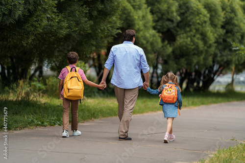 loving family. a caring dad accompanies cheerful children, a boy and a girl with backpacks, to school, Back to school. the first day of training © skif
