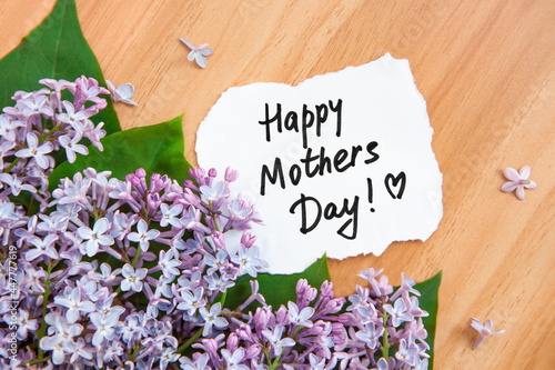 Happy mothers day - card with bouquet of lilac flowers and text on wooden background, congratulation
