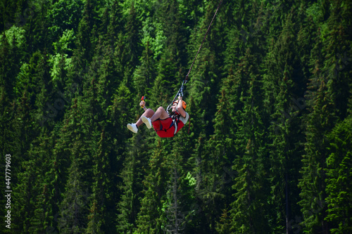 A young man jumped from bungee jumping and now hangs on a rope and films himself on a sports video camera against a blurred background of a green forest