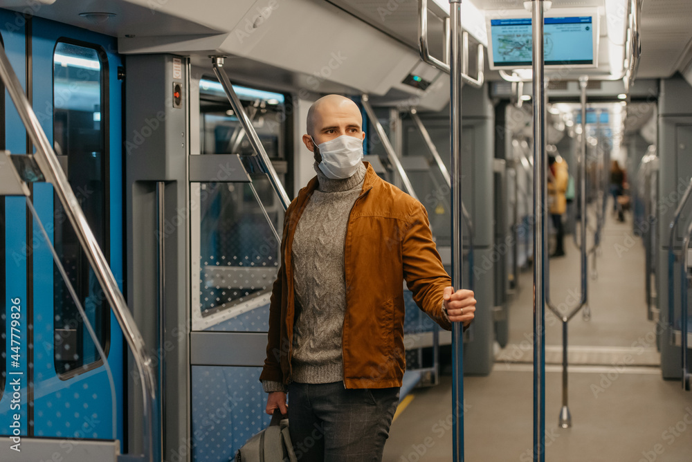 A bald man with a beard in a face mask is holding the handrail in a subway car.