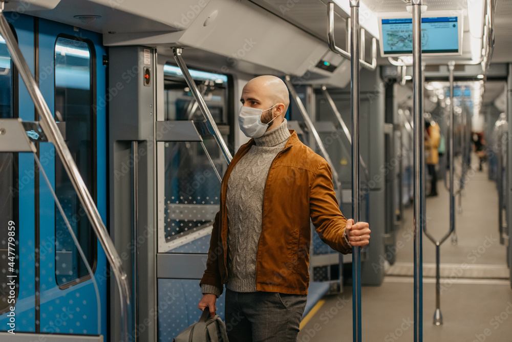 A bald man with a beard in a face mask is holding the handrail in a subway car.