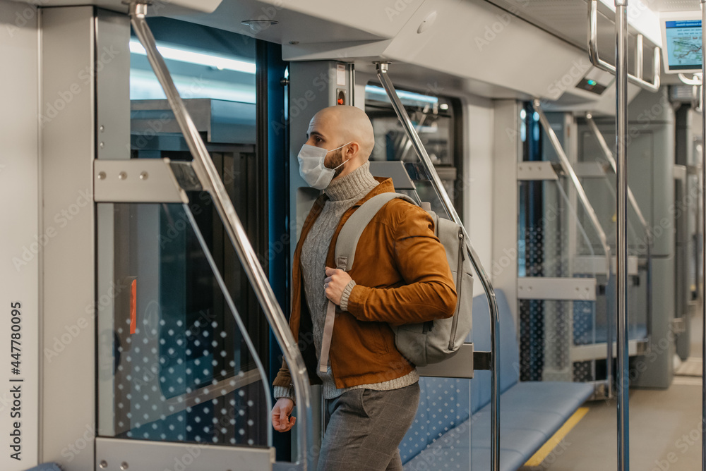 A bald man with a beard in a face mask is leaving a subway car.