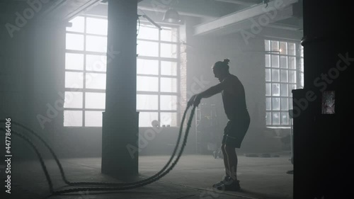 Guy battling ropes during training session. Sportsman performing intense workout photo