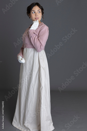 A Regency woman wearing a printed cotton dress and a pink linen spencer with gloves