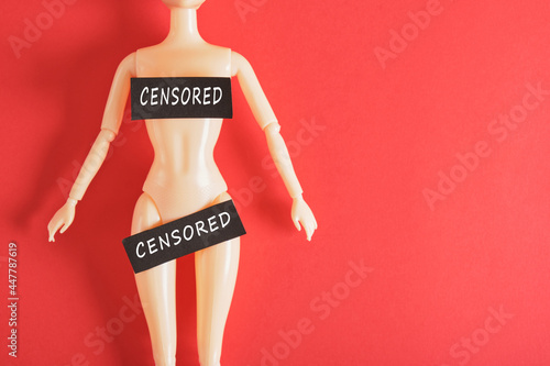 the body of a naked doll on a red background, the inscription on a black plate is censored