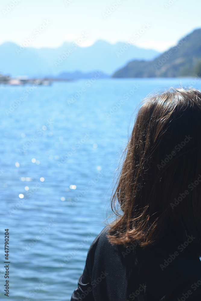 young woman with black hair from behind looking at the water of a lake and the sun young woman with black hair from behind looking at the water of a lake and the sun