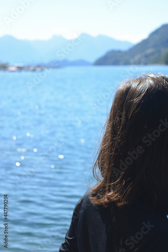 young woman with black hair from behind looking at the water of a lake and the sun © Lautaro