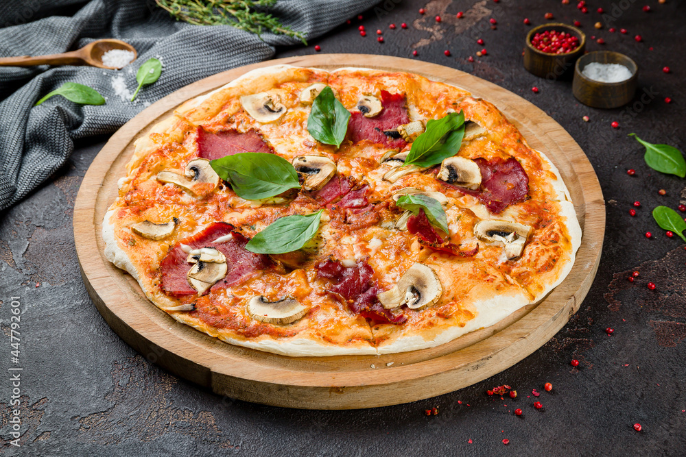 Pizza with ham and mushrooms on the board on dark concrete table