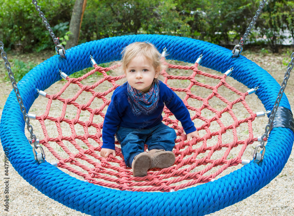 Cute little child having fun on a colorful swing outdoor in the park. Beautiful spring day in children playground Cute little child having fun on a colorful swing outdoor in the park. Beautiful spring day in children playground