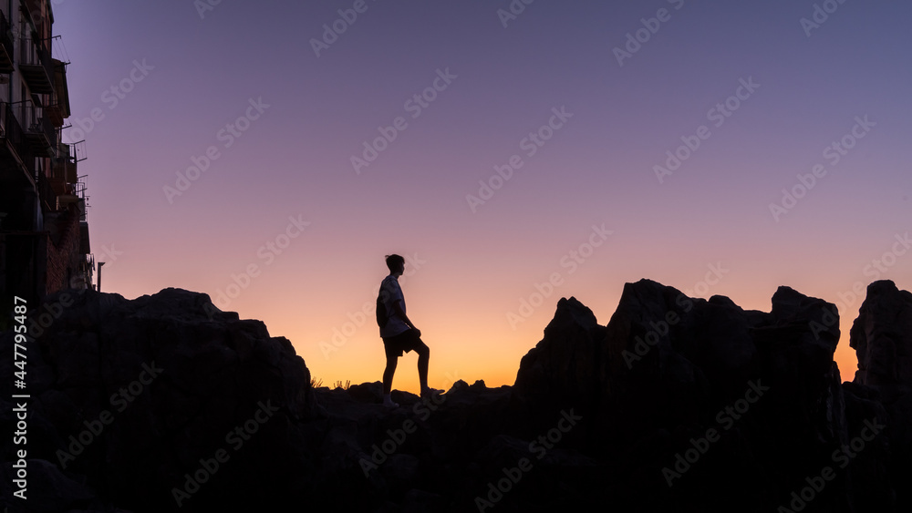 young man standing on rock looking straight. Nature and beauty concept. Orange sundown. silhouette at sunset.