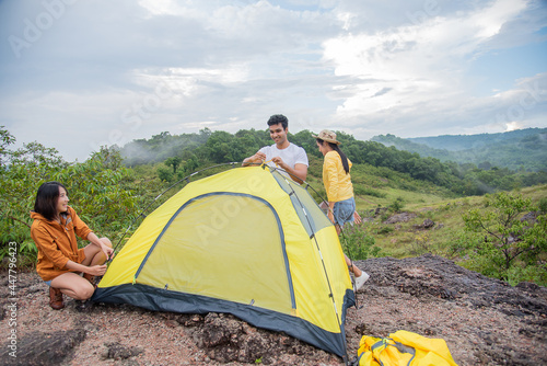 group of male and asian female friends are pitching tents among the beautiful mountains