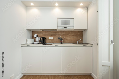 Front view of small kitchen in white and oak wood tones, microwave and accessories included in a holiday rental apartment