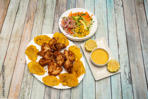 Typical Caribbean dish of picatodo cooked in an Ecuadorian restaurant with chili sauce, battered fixed chicken thighs, pieces of fried ripe banana and vegetable salad with sweet corn photo