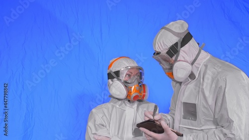 Scientist virologist in respirator makes write in an tablet computer with stylus. Man and woman wearing protective medical mask. Health safety virus coronavirus epidemic 2019 nCoV. Chroma key blue. photo