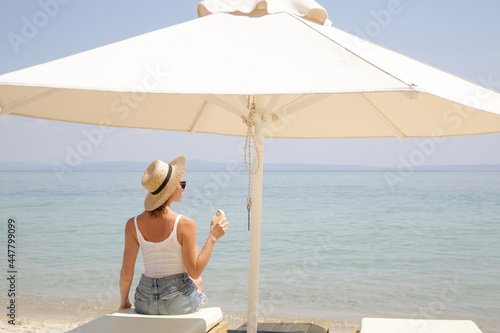 Young woman with straw hat holding a glass of cocktail and looking at the horizone over the sea. Idyllic summer vacation concept. photo