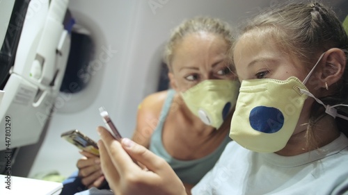 Family woman and child baby travel tourist caucasian at plane aircraft with wearing protective medical mask. Read shock news about coronovirus at smartphone mobile. Virus epidemic sars-cov-2 covid-19.