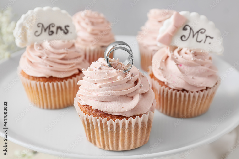 Dessert stand with tasty cupcakes and wedding rings, closeup