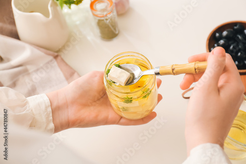 Woman taking piece of tasty feta cheese from jar on table in kitchen, closeup